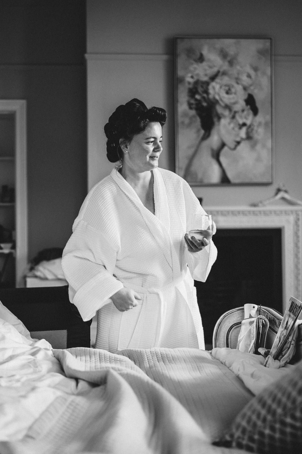 A person wearing a white bathrobe stands in a bedroom setting while looking to the side in black and white photography.