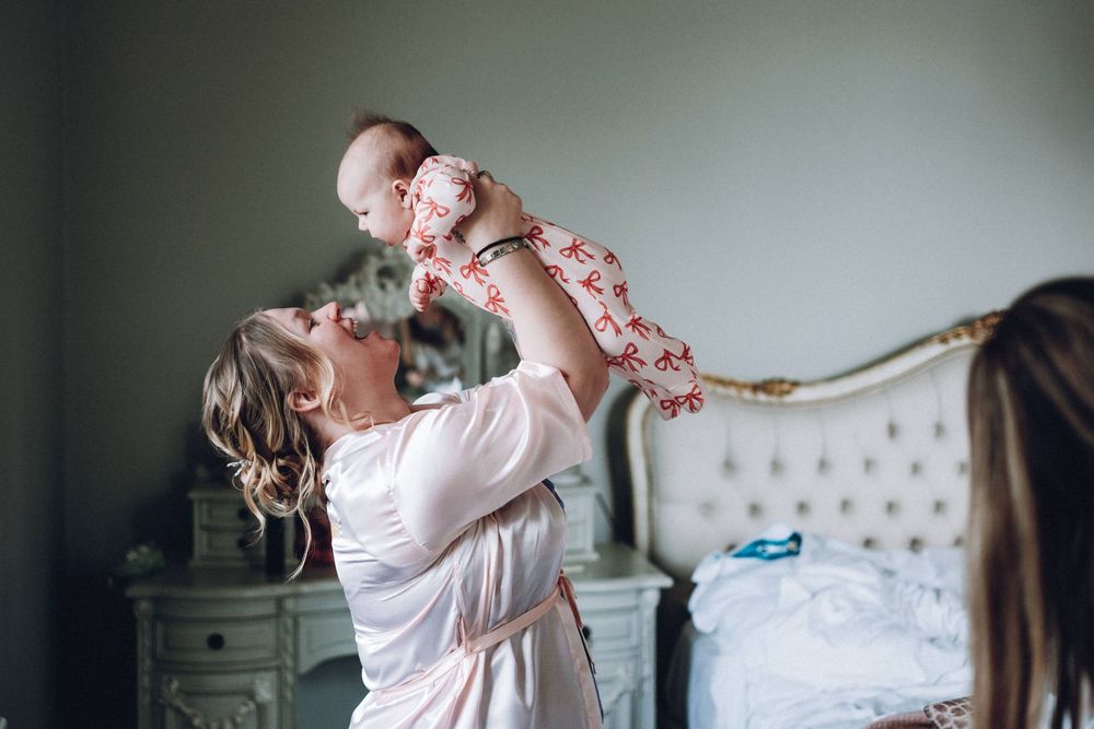 Parent lifting up baby while playing together in a cozy bedroom with tufted headboard and side table.