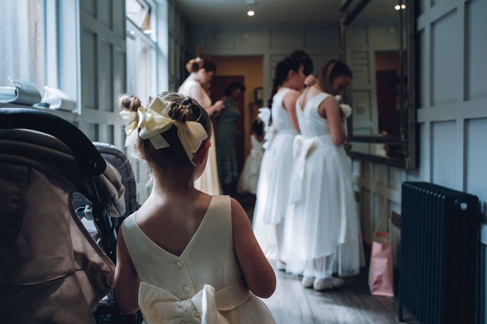Bride in white wedding dress getting ready in hotel room with bridesmaids assisting before ceremony.