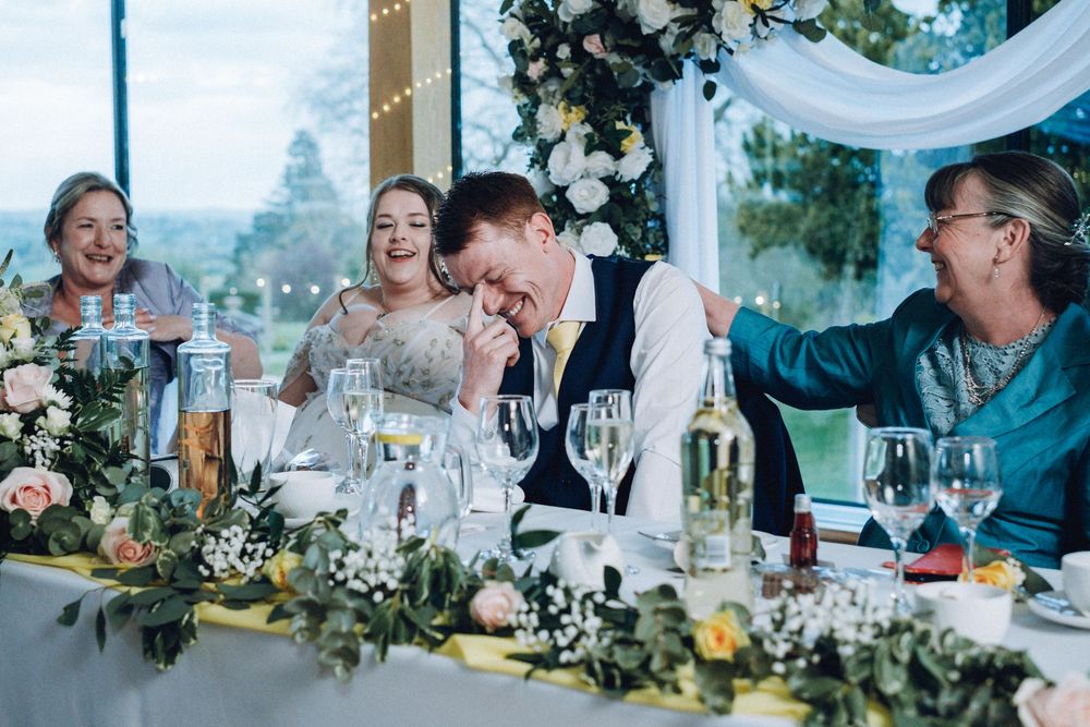 Wedding reception guests seated at elegant tables with white draping and greenery decorations enjoy dinner and conversation.