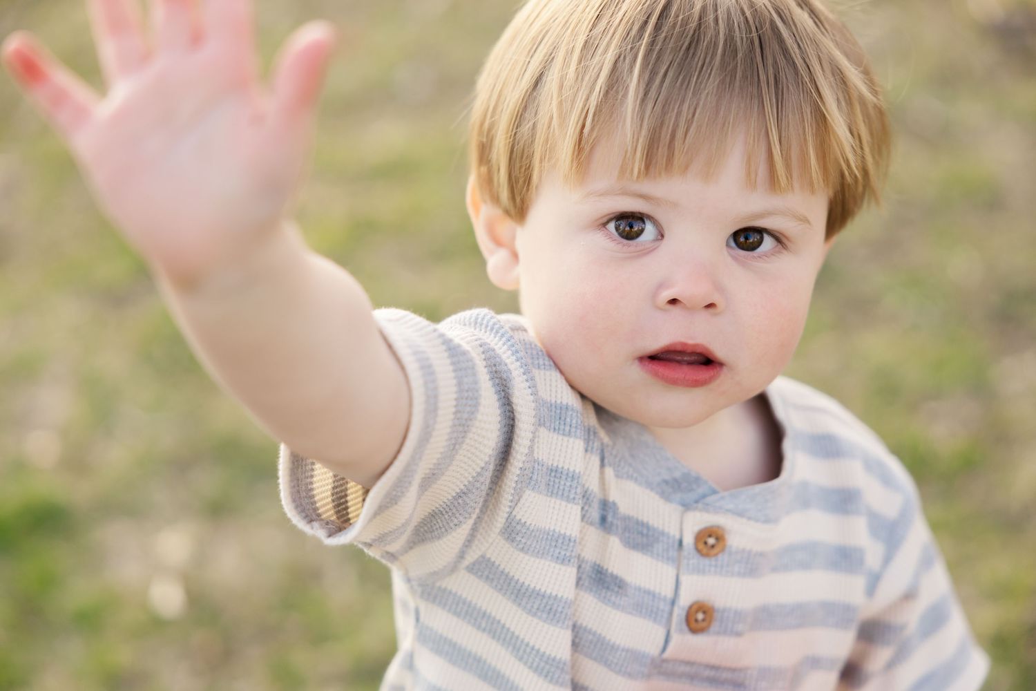 Child in striped shirt reaching up with one hand against blurred nature background. Family mini session.