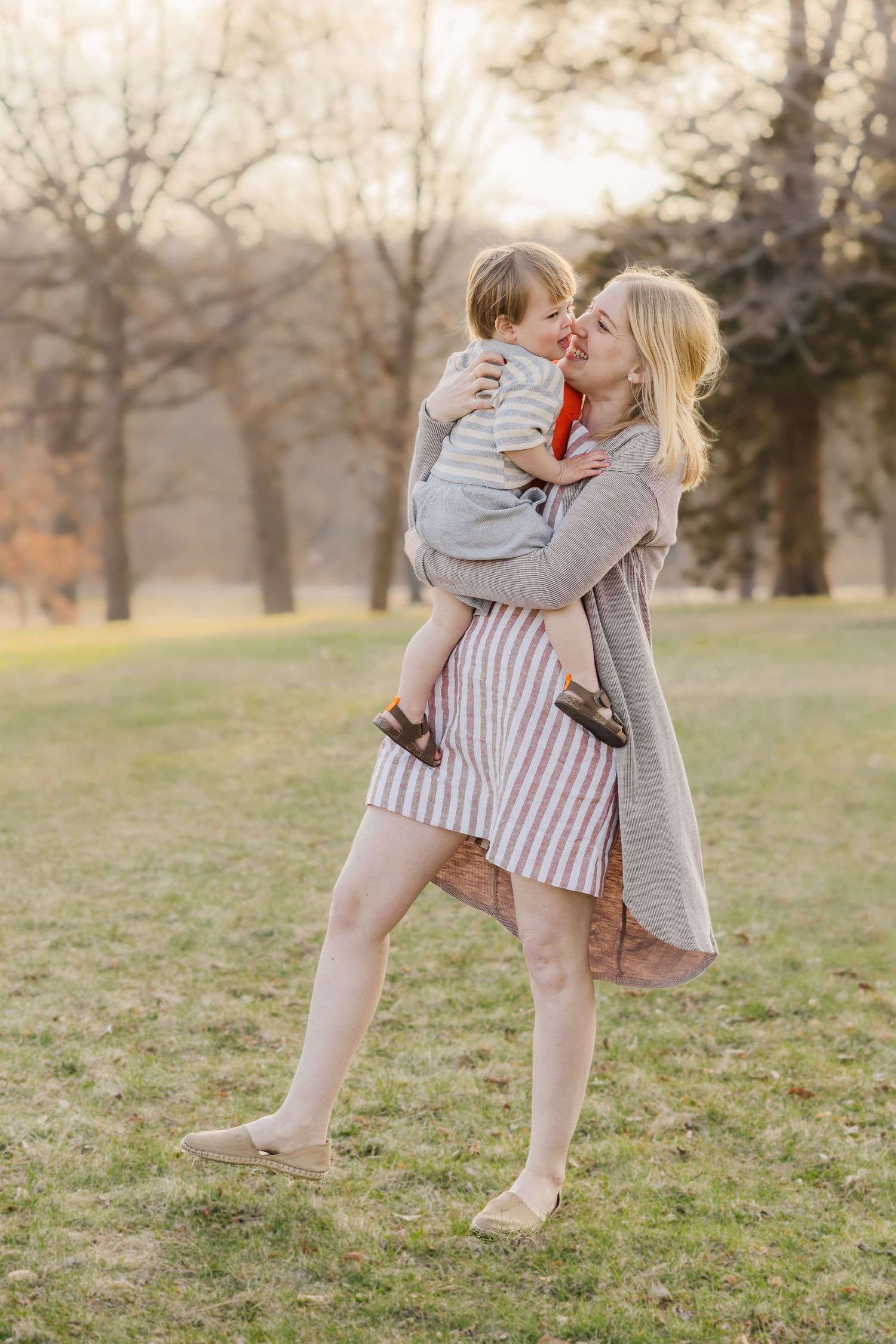 Tender moment captured in golden hour light on grassy field. Mother's Day photoshoot.