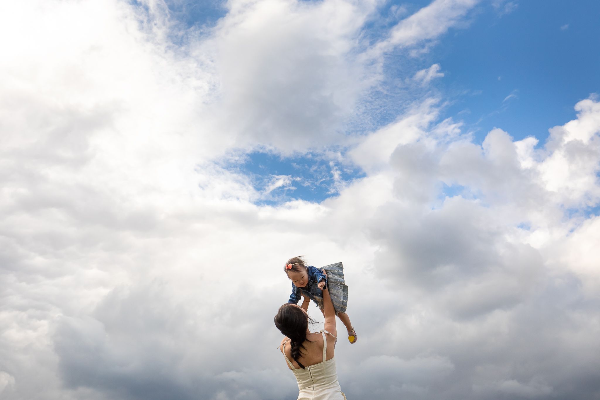 A silhouetted figure lifts a small child against a dramatic cloudy blue sky backdrop.