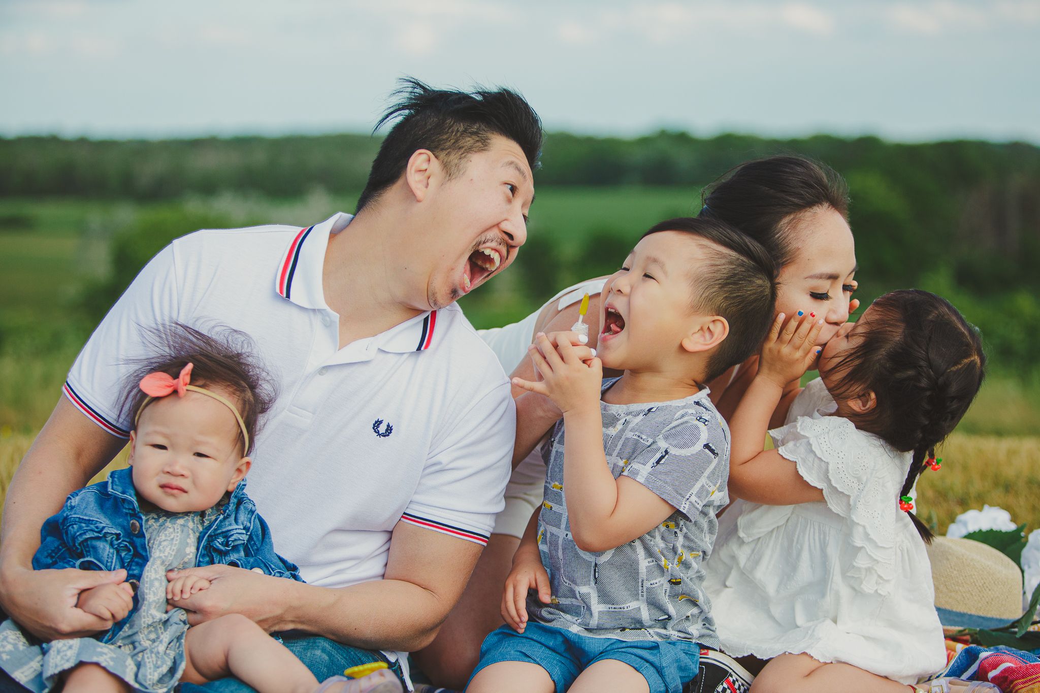 A joyful family sits together outdoors in a grassy field, laughing and sharing a candid moment together.