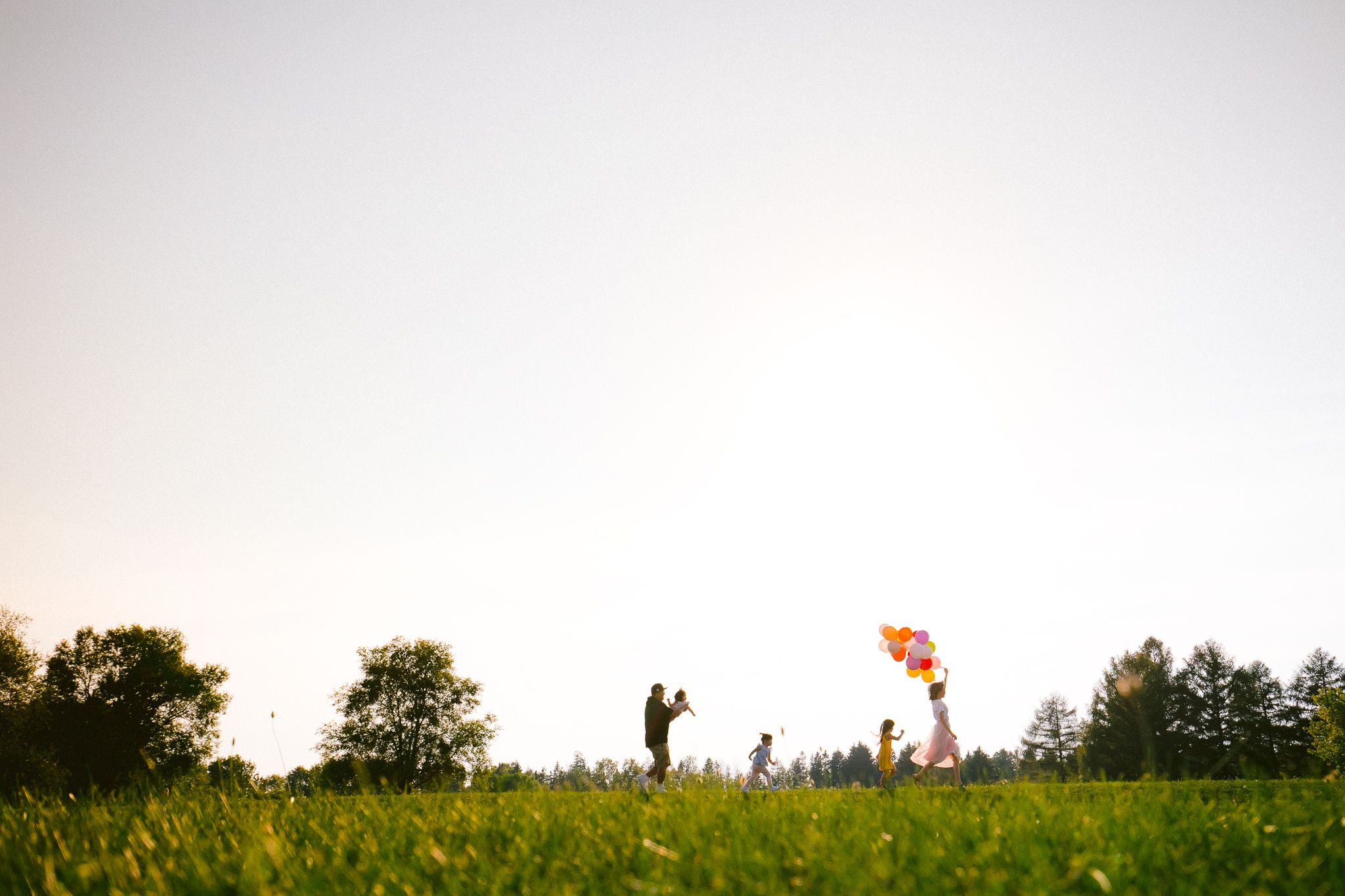 Silhouettes of people standing in a grassy field at dusk with vibrant orange sky and trees in background.
