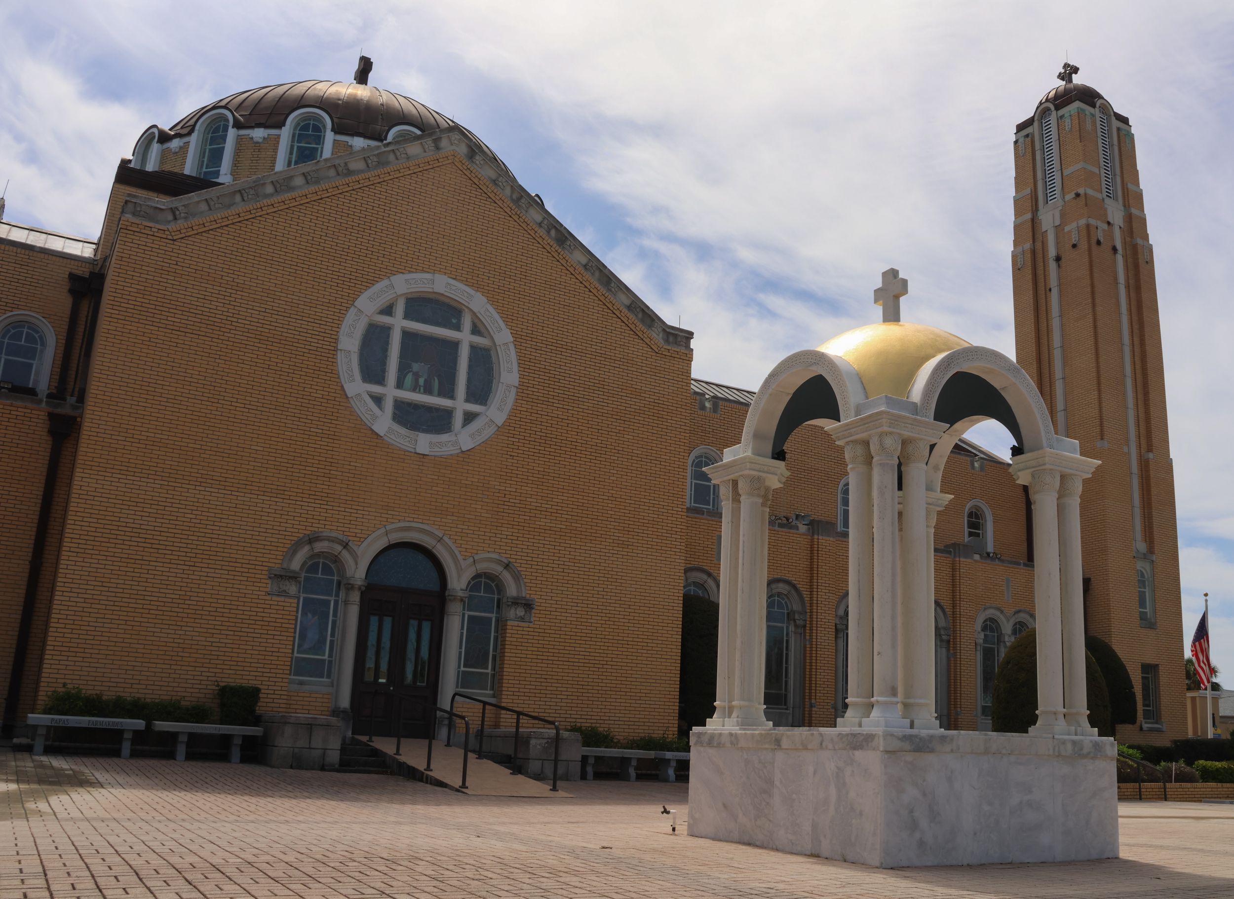 A tan Spanish mission-style church with a bell tower and white arched entrance sits beneath a bright blue sky.