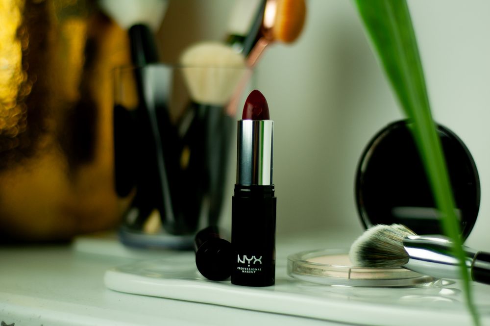 Black NYX lipstick displayed on vanity with makeup brushes and green plant. Product photography, San Diego, California
