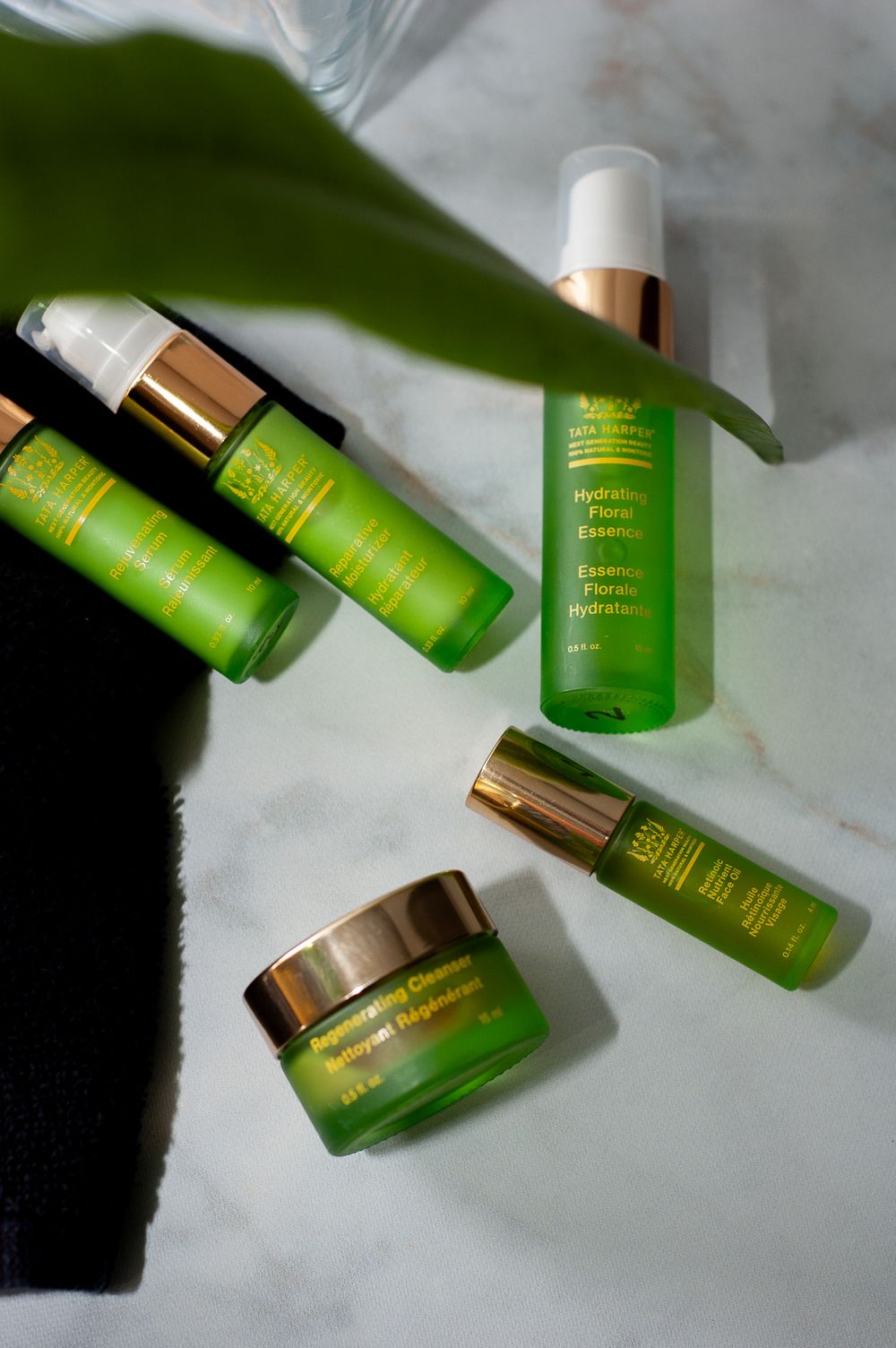 Collection of green skincare products and bottles arranged with plant leaf on white surface. Product photography, San Diego, California