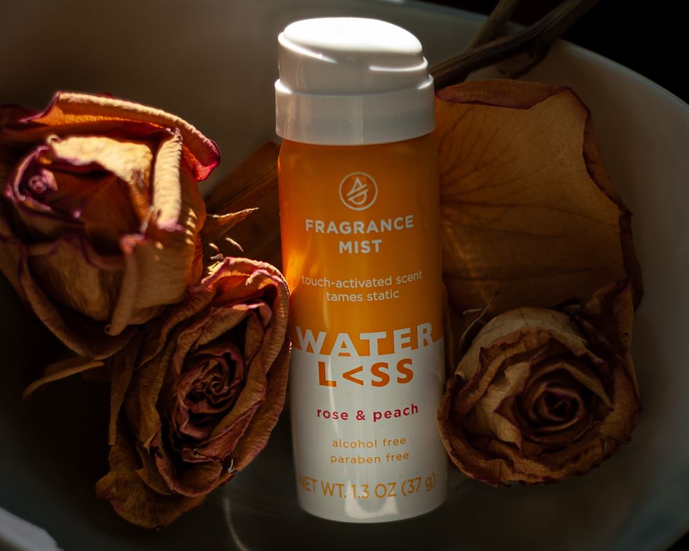 Orange Waterless rose and peach fragrance mist bottle displayed with dried roses in moody lighting. Product photography, San Diego, CA