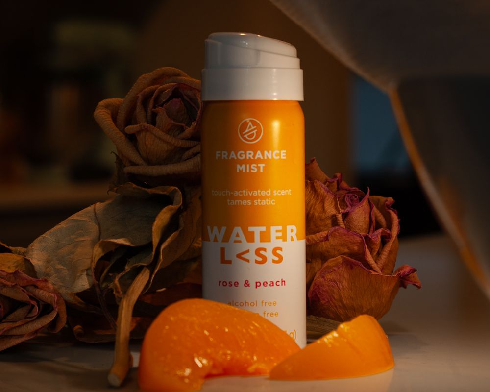 Fragrance mist bottle surrounded by dried roses and fresh orange slices in atmospheric lighting. Product photography, San Diego, California