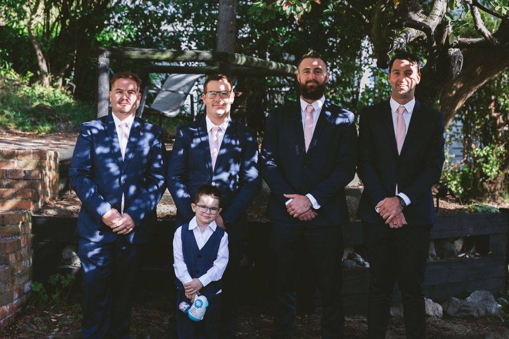 Groomsmen and young ring bearer posing together outdoors in formal attire.