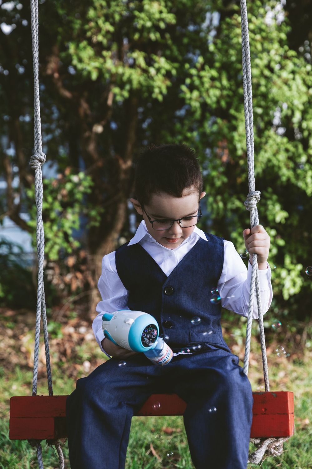 Young attendant in formal vest sits on red swing holding blue water bottle.