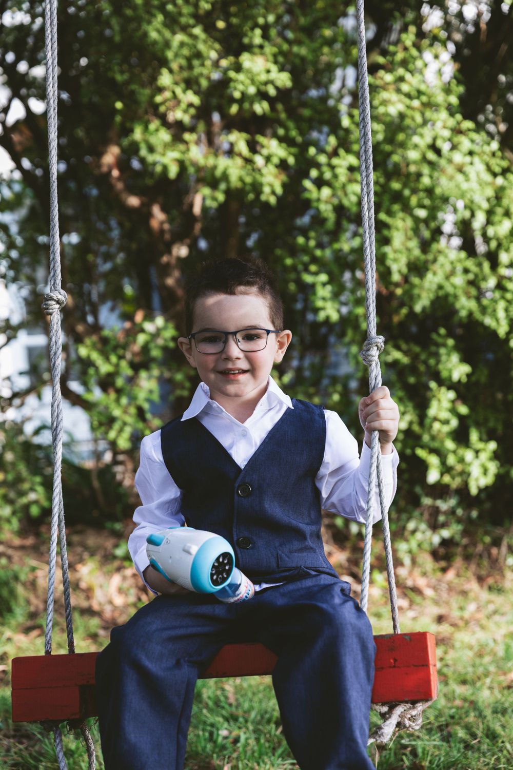 Child in formal attire smiles while sitting on red wooden swing.