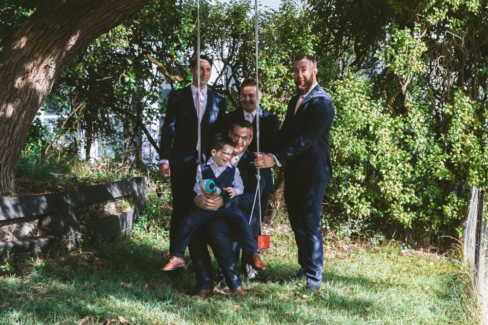 Group photo with ring bearer on swing surrounded by wedding party members.