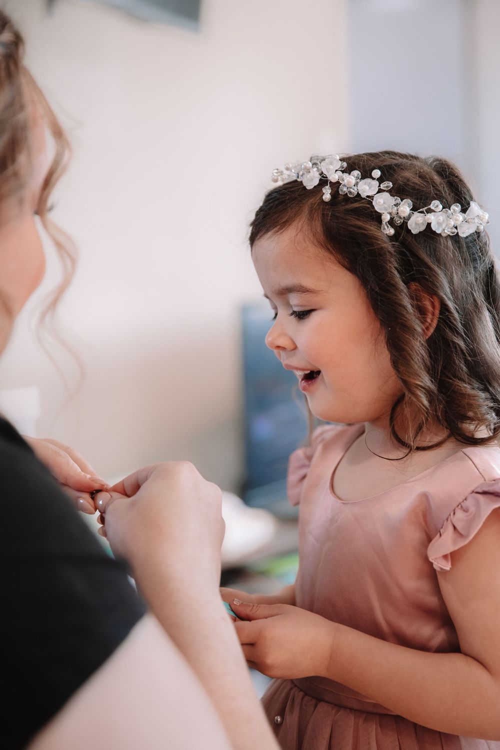 A delighted child in a pink dress and floral crown interacting with someone off-camera.