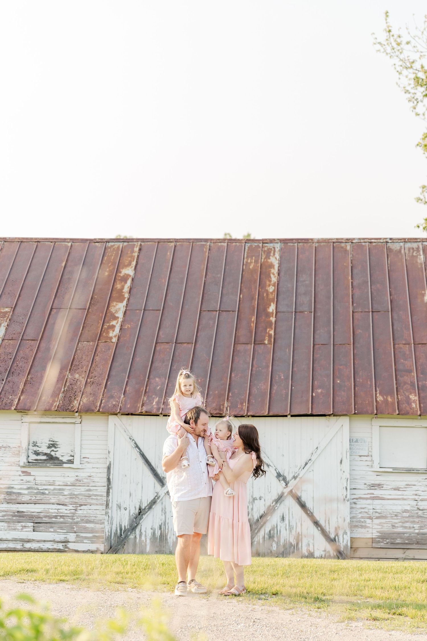A group of children playing together outside a rustic white barn on a sunny day.