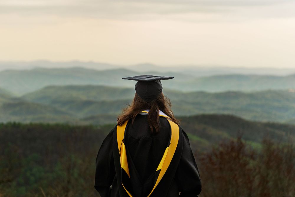 Silhouette of graduate in cap and gown against mountain vista backdrop.