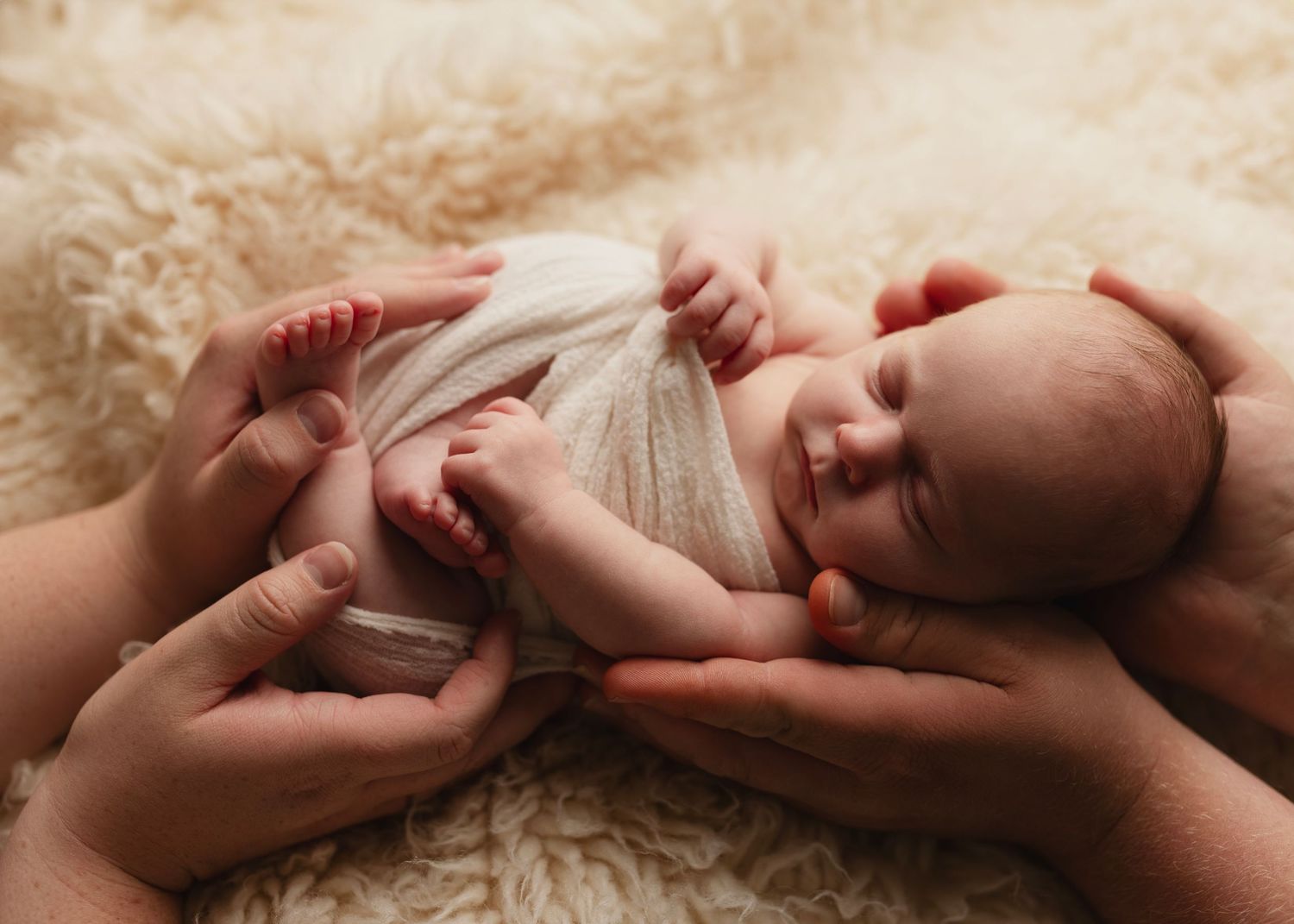 Kathleen sleeps held safely in her mother and father's hands on a fluffy blanket. Elizabeth Lang Photography Surrey