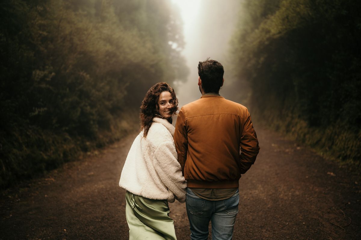 Couple walking down a foggy forest path together in moody autumn atmosphere with brown and green tones.