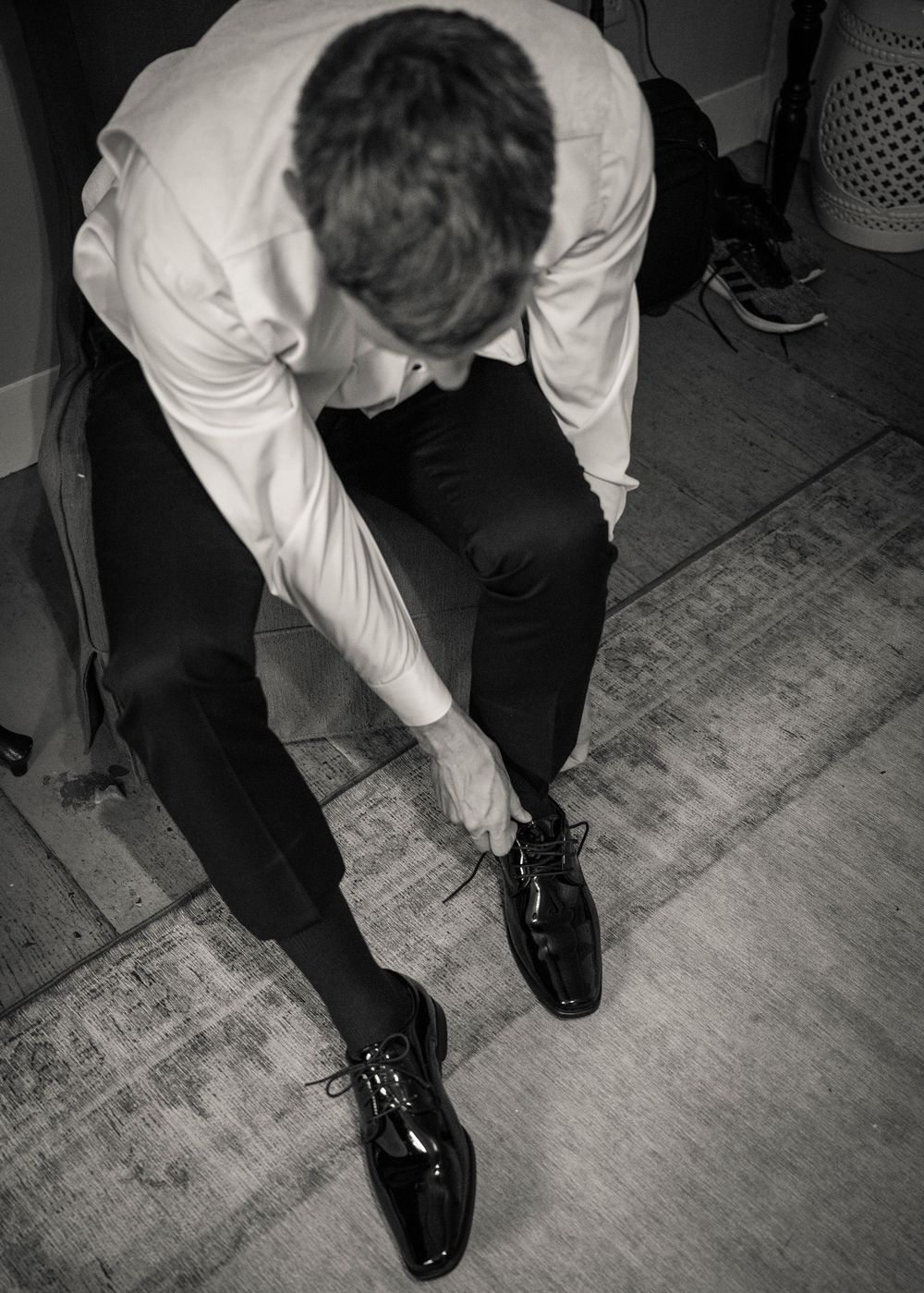 Black and white image series showing someone in a white shirt bending down to adjust or fix their black dress shoes.