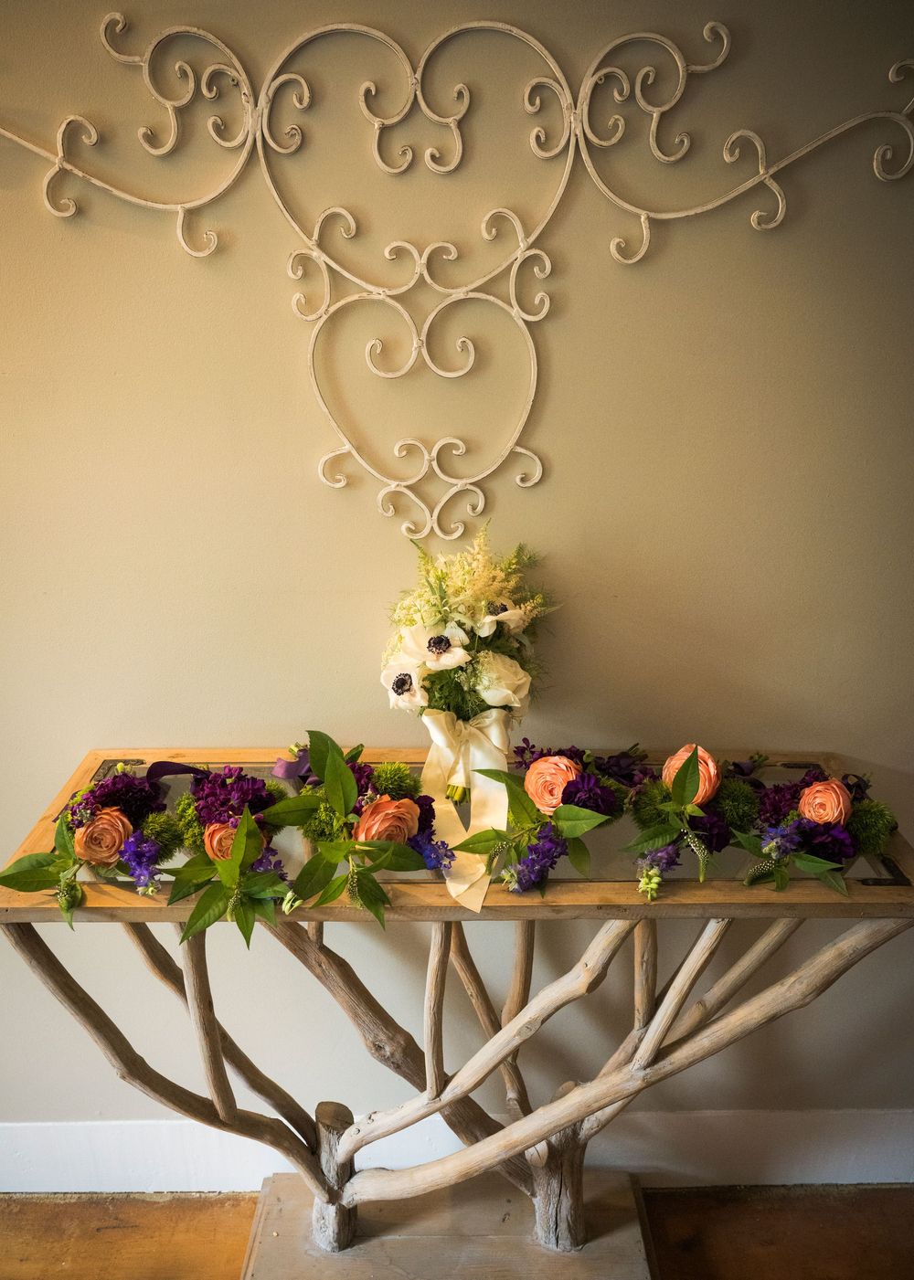 A creative wall-mounted branch shelf decorated with colorful floral arrangements and greenery in different stages of assembly.