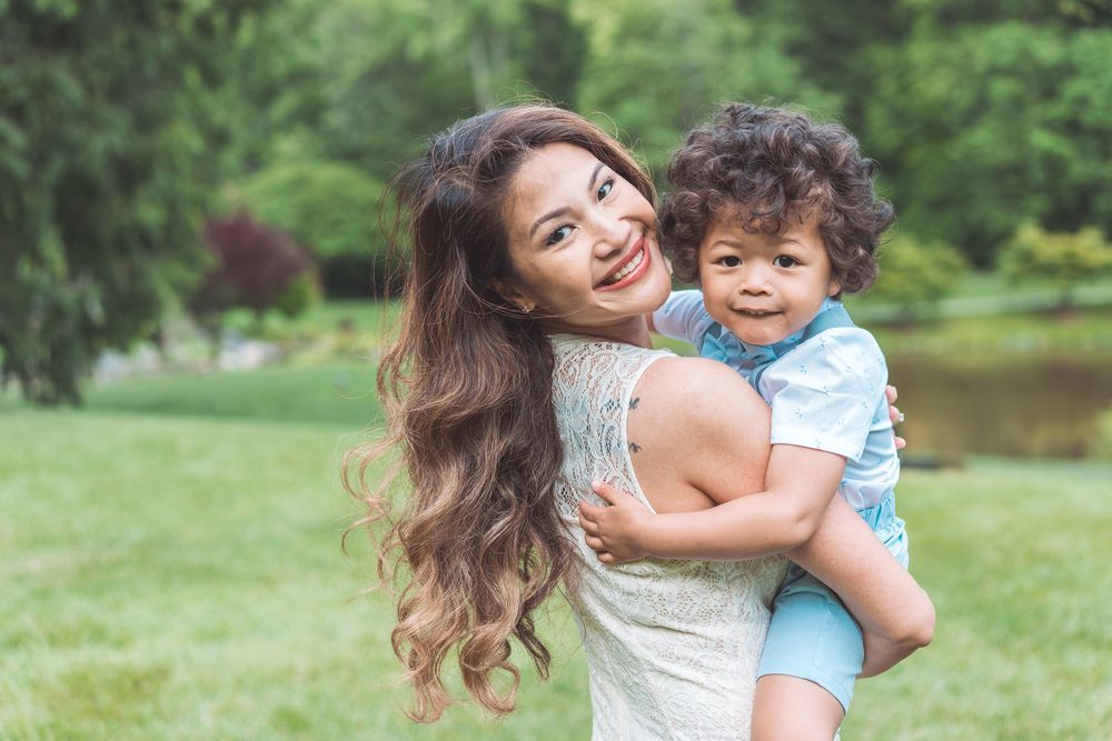 Parent and child share joyful laughter while embracing in a sunny garden setting.