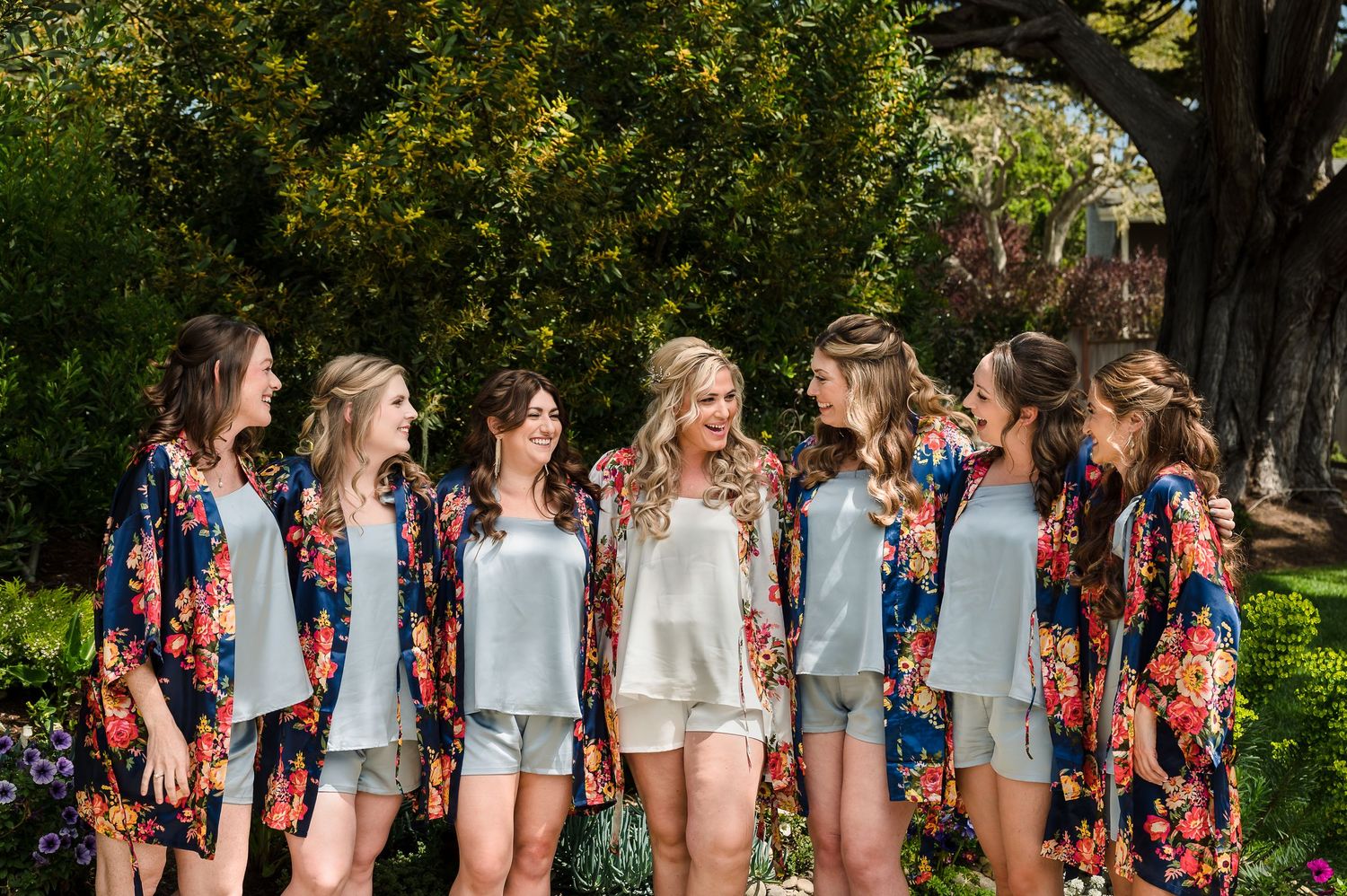 A group of friends in coordinated outfits stand together in a summer garden setting for casual photos.