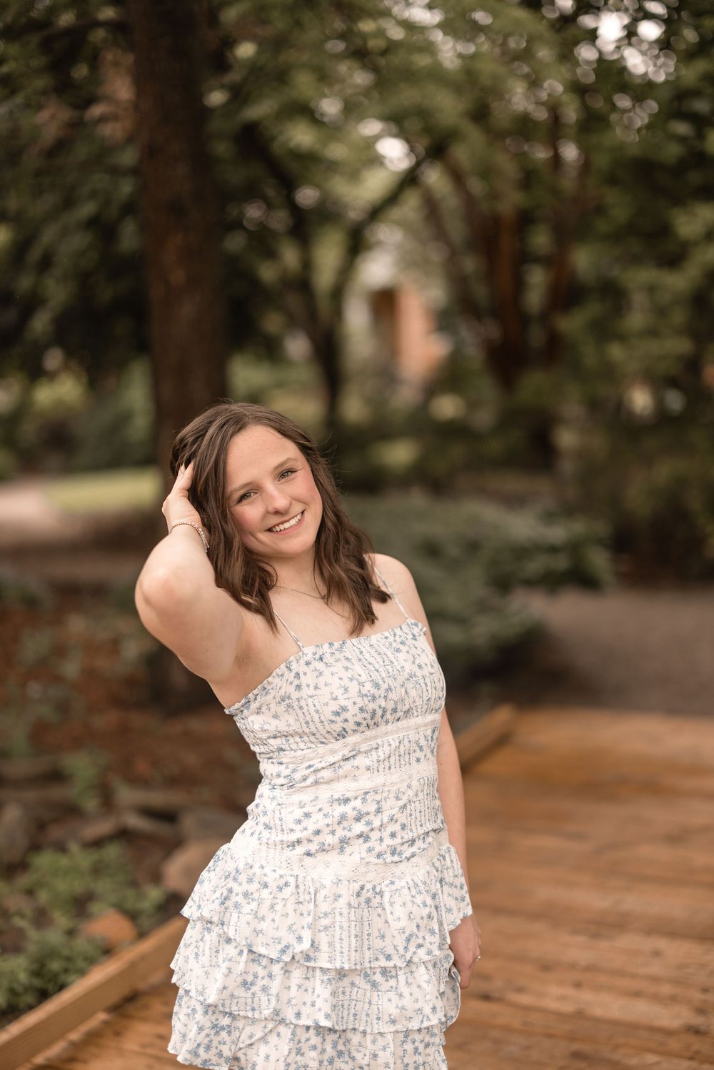 A white tiered ruffle dress being worn while standing on a wooden pathway surrounded by lush greenery.