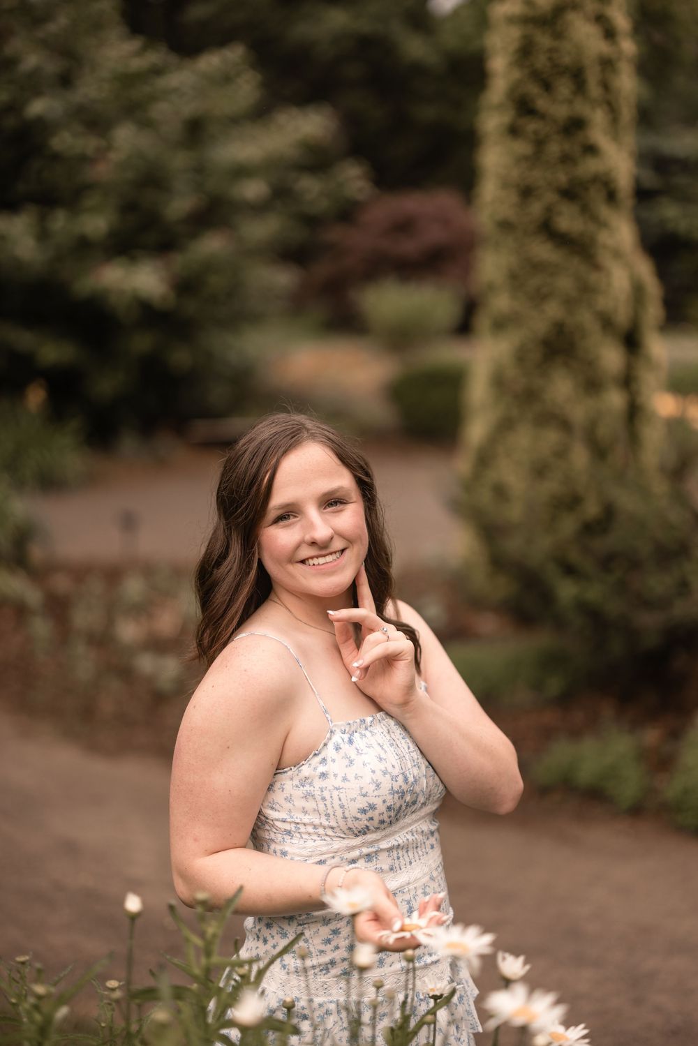 Someone poses in a white beaded strapless dress along a garden path surrounded by lush greenery.