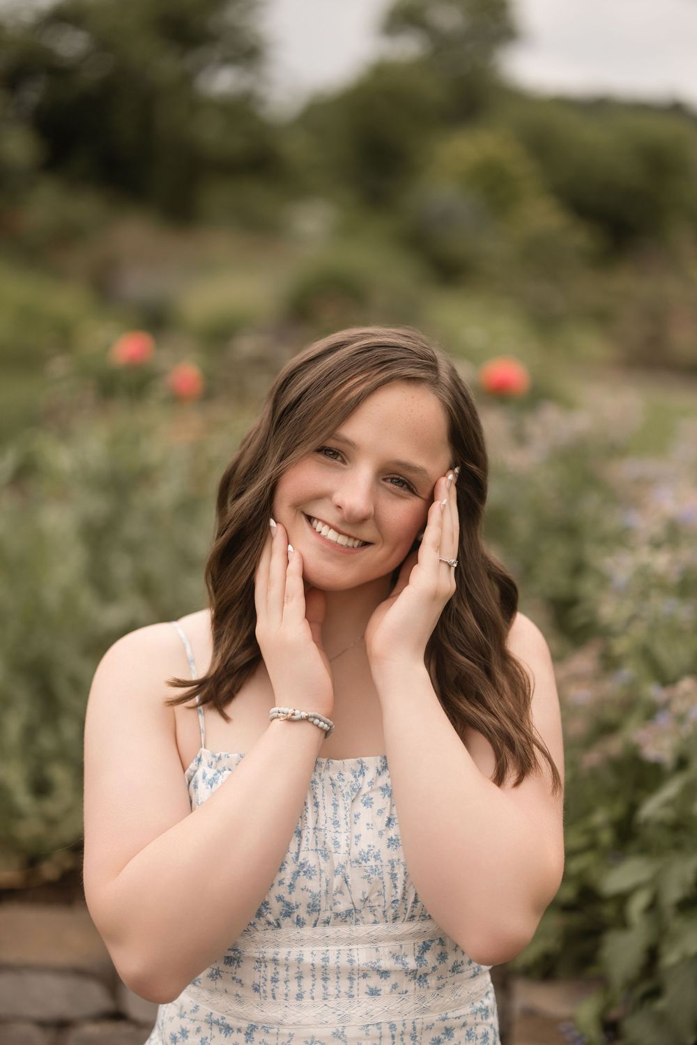 A smiling woman in a floral dress poses outdoors in a garden with orange flowers in the background.