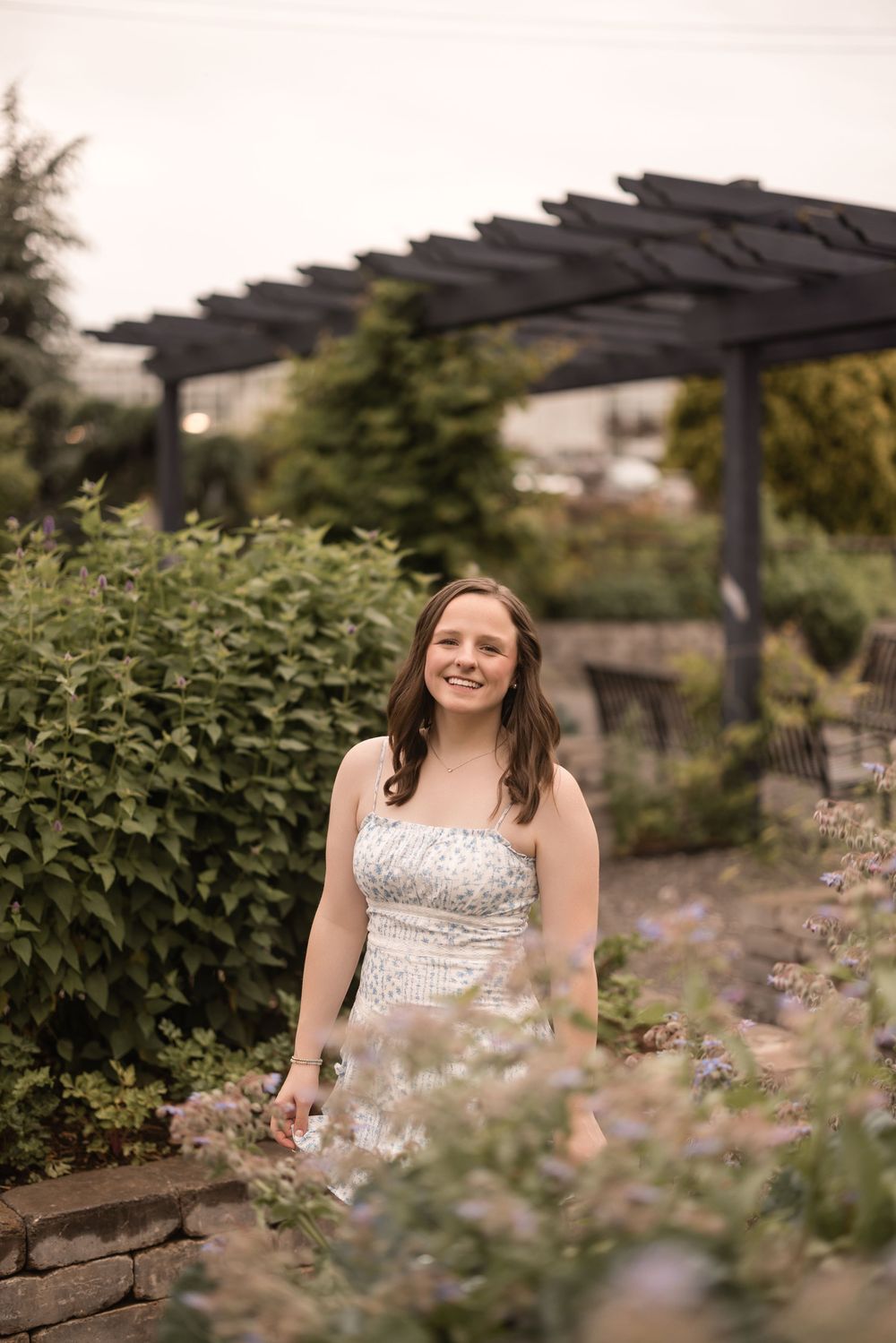 A white strapless dress in a garden setting with a wooden pergola and blooming flowers in the background.