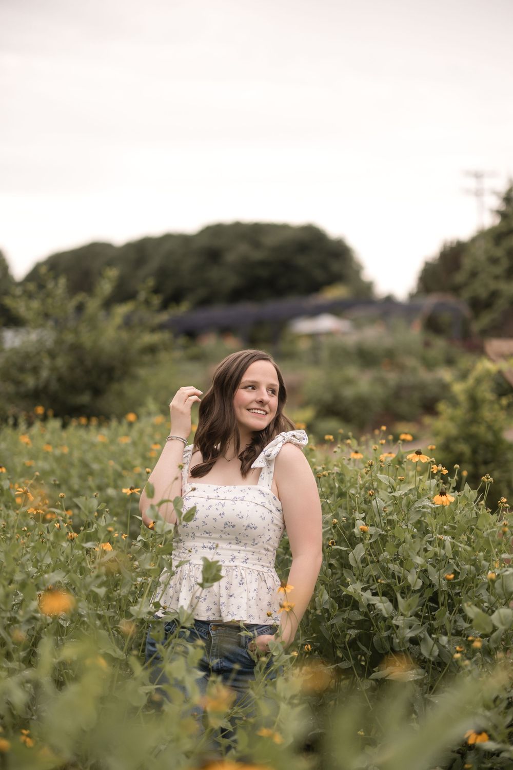 A woman in a white top poses in a field of wildflowers on a sunny afternoon.