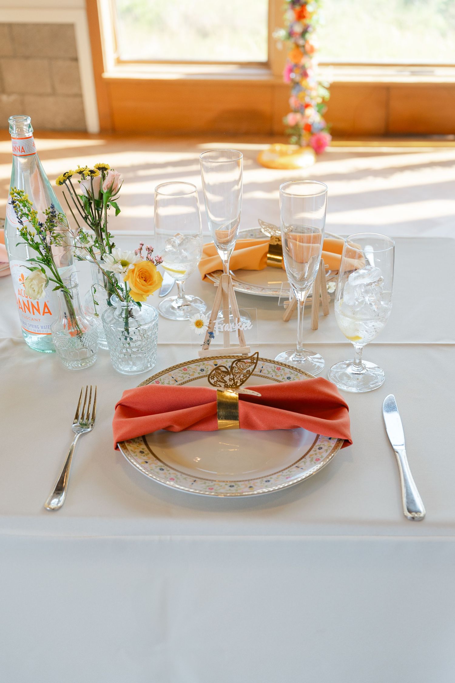 An elegant table setting at a wedding reception with coral napkins, crystal glassware, and delicate floral arrangements.