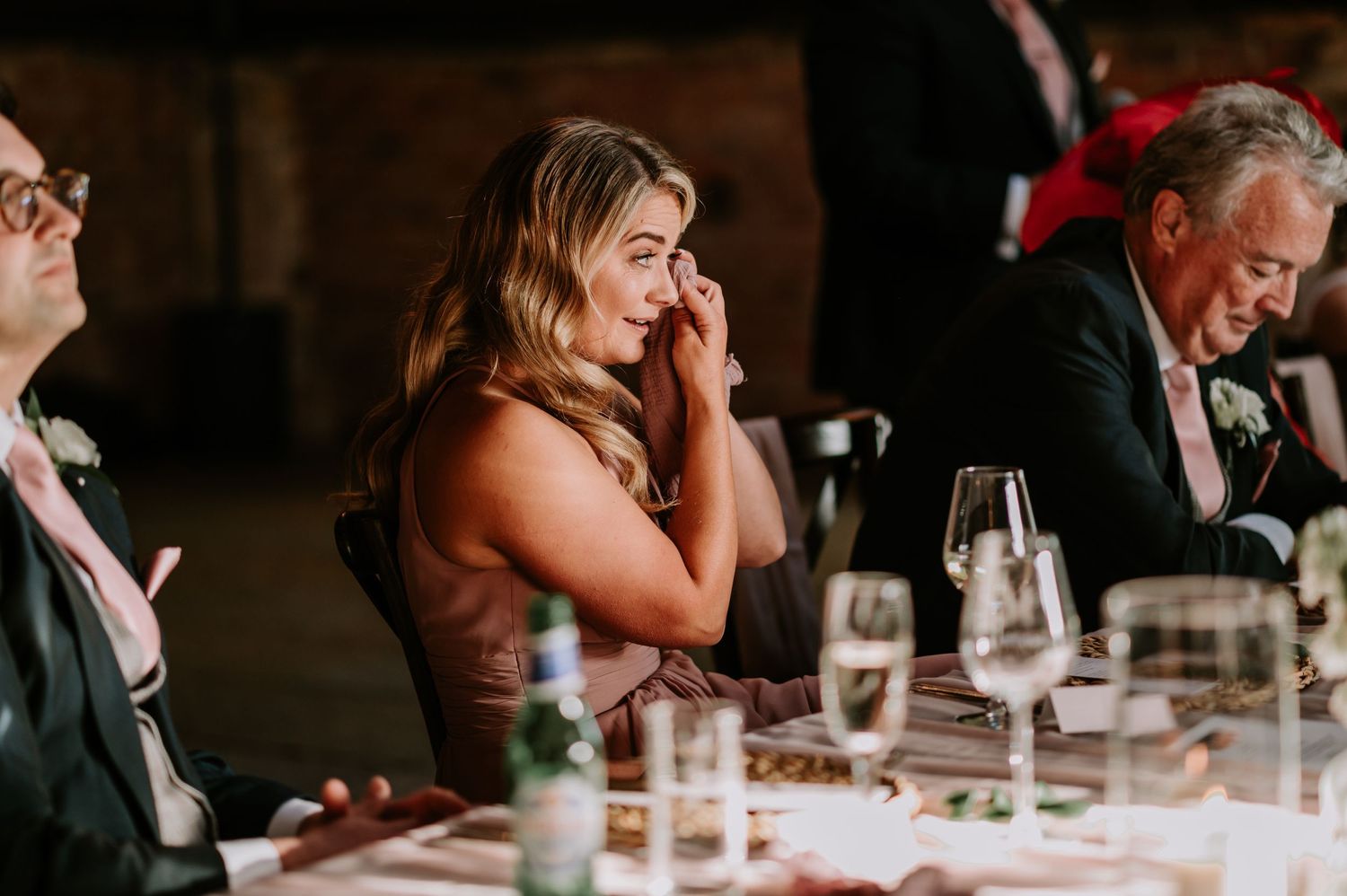 Bridesmaid wiping a tear during the speeches at a wedding, caught in a moment of emotion.