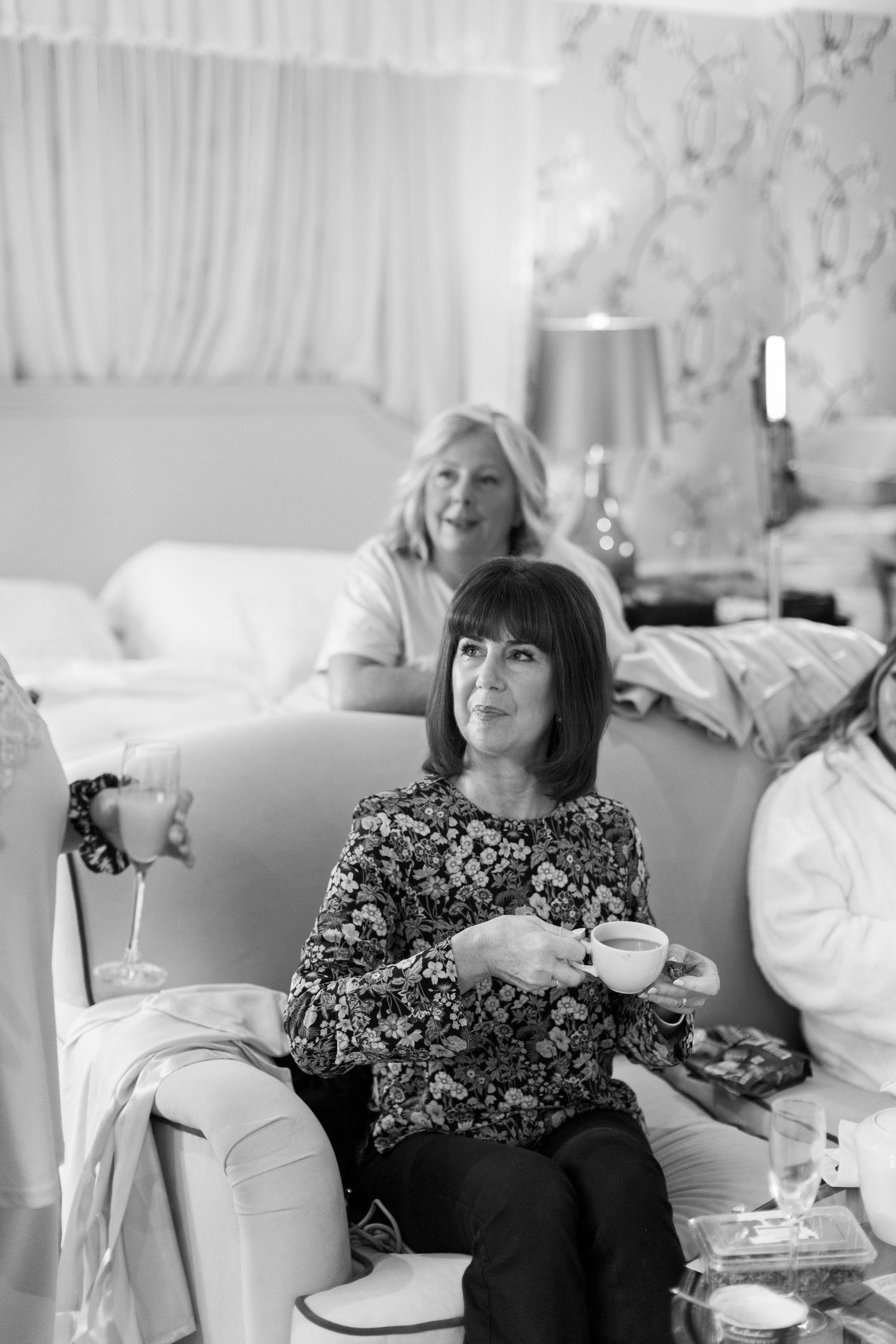 A black and white photograph of two mums relaxing on a sofa with cups and drinks during wedding morning at ellenborough park cotswolds