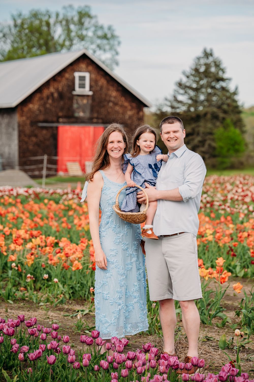 A family stands together in a colorful tulip field with rustic farm buildings in the background.