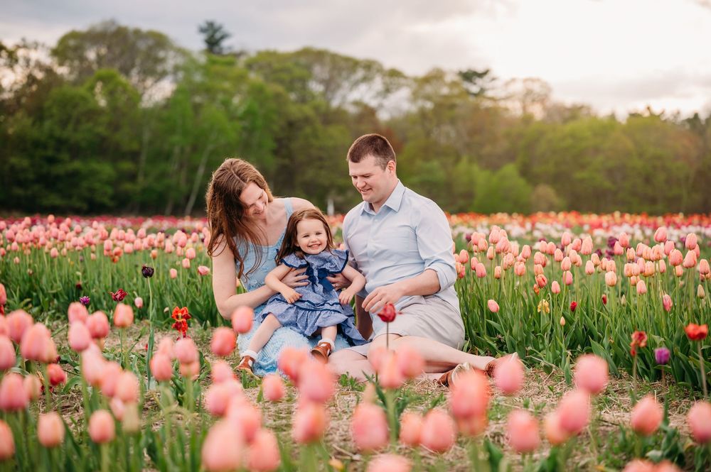 Three people sit together among vibrant pink tulips in a garden field during golden hour.