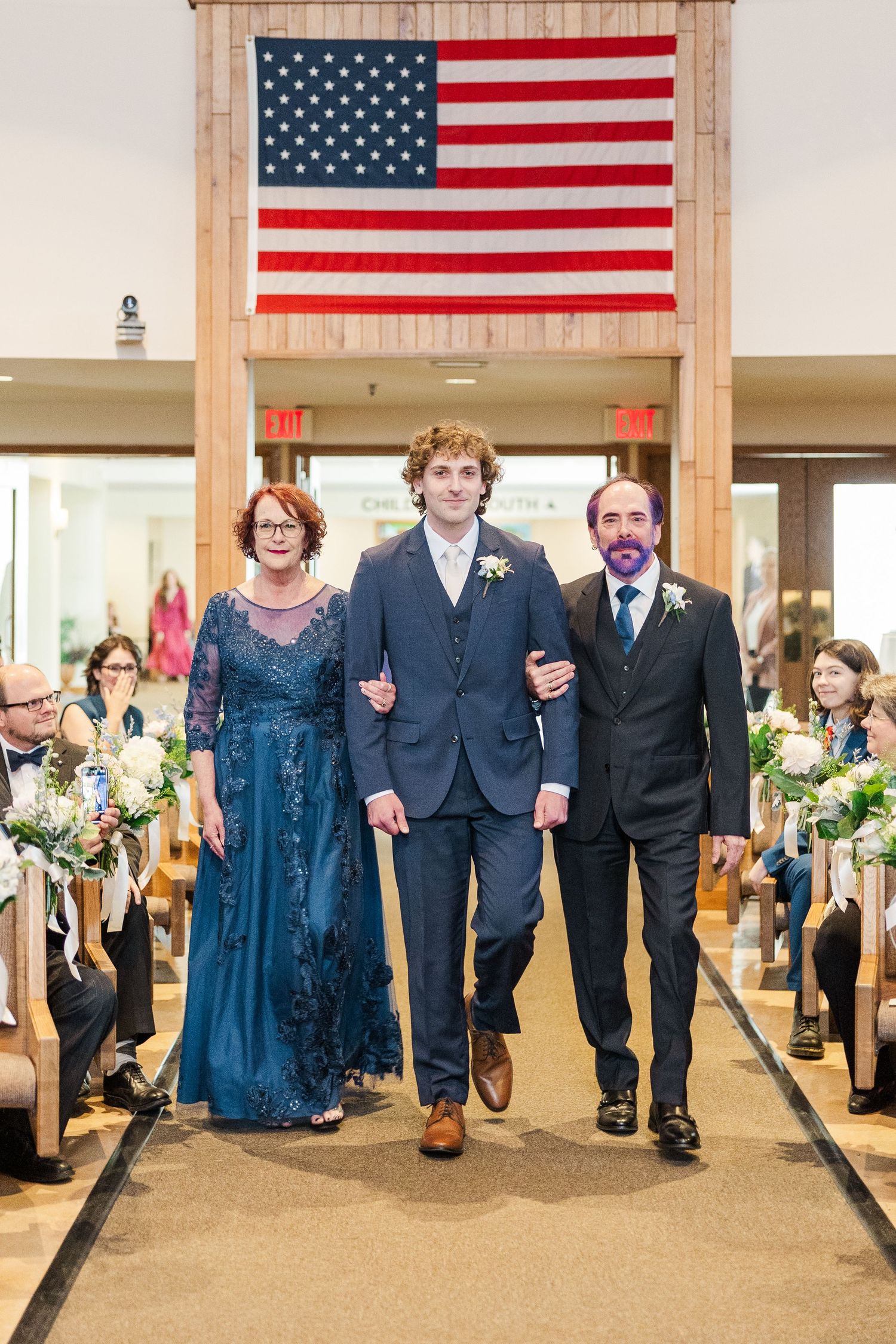 Members of a wedding party walk under a framed American flag during a ceremony at an indoor venue.