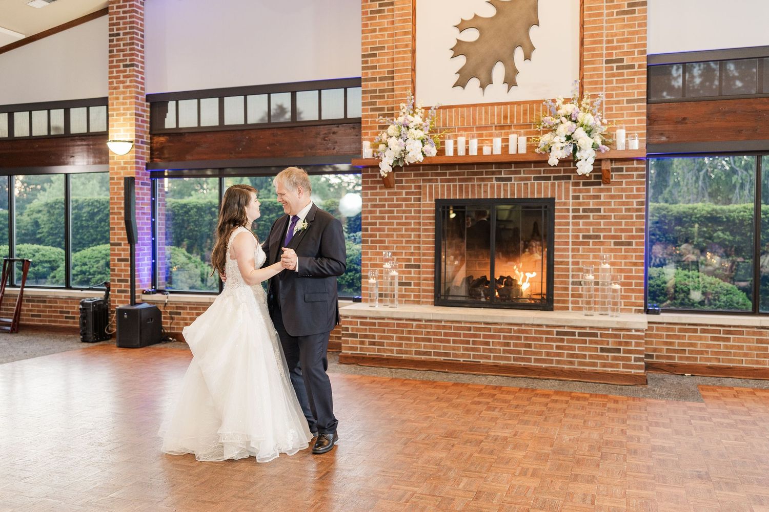 A couple shares an intimate dance in a rustic venue with exposed brick fireplace, parquet floors and elegant lighting.