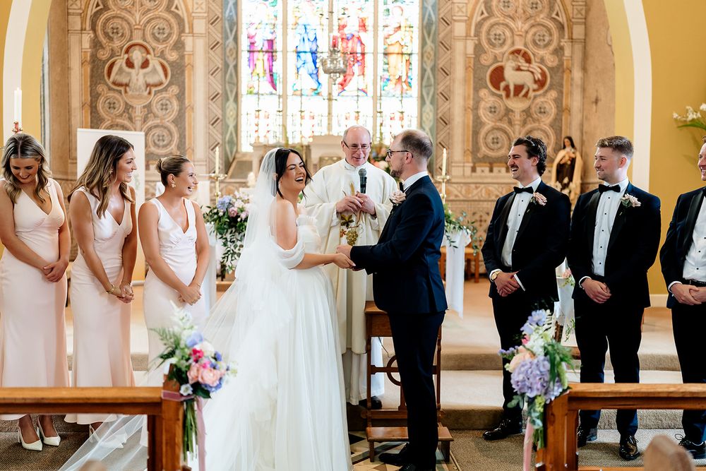 Wedding ceremony taking place in a beautiful church with stained glass windows and people gathered at the altar.