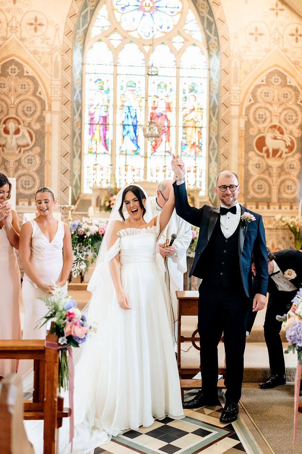 Newlyweds celebrate joyfully in a grand church with stained glass windows and ornate Gothic architecture during ceremony.
