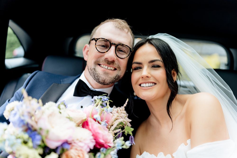 A happy newlywed couple smiling together in a car after their wedding ceremony.