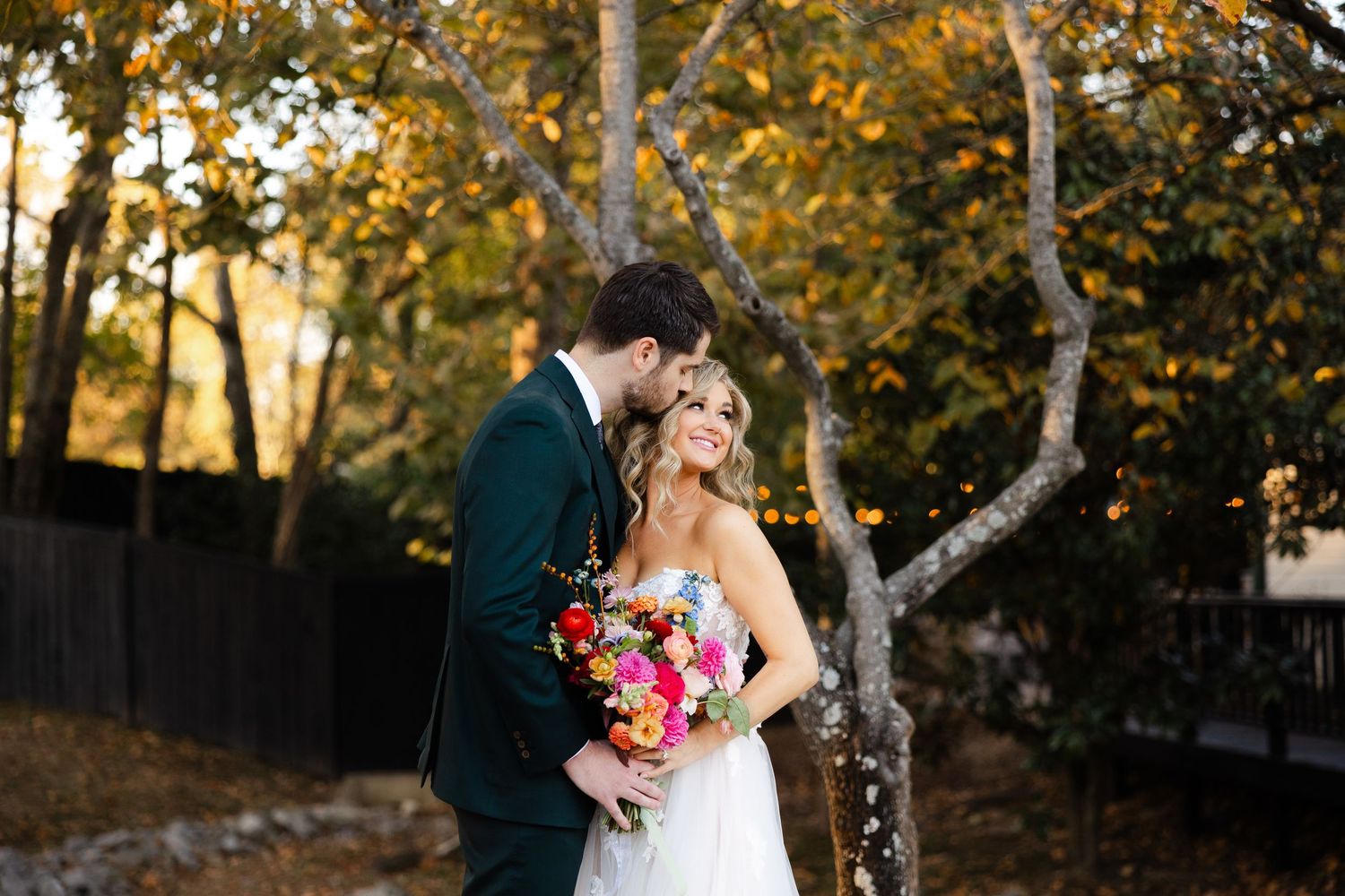 A romantic outdoor autumn wedding photo with birch trees and golden sunlight filtering through colorful fall foliage.