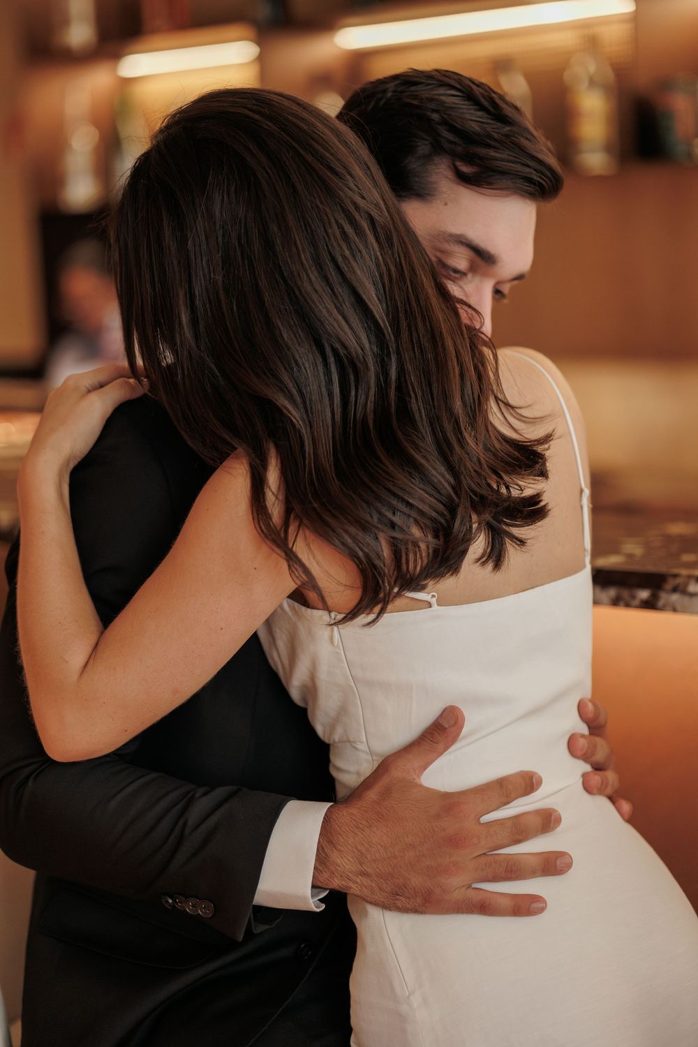 A couple in formal attire share an intimate embrace at what appears to be a wedding or formal event.