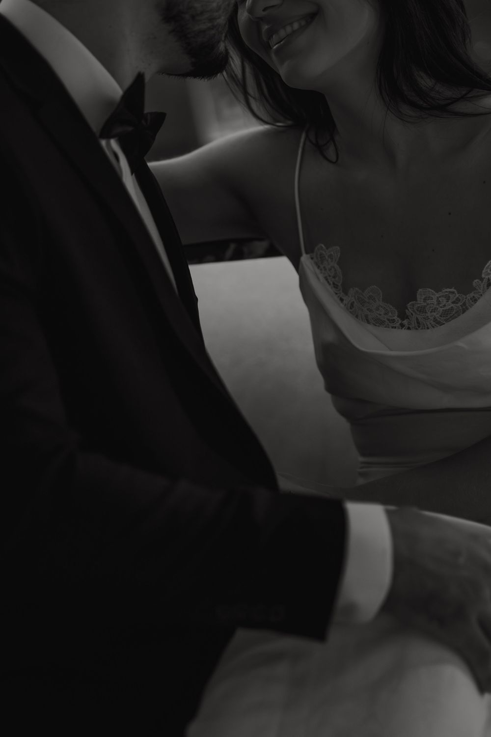 Black and white intimate photo showing couple embracing, with woman in lace cami and man in formal suit.