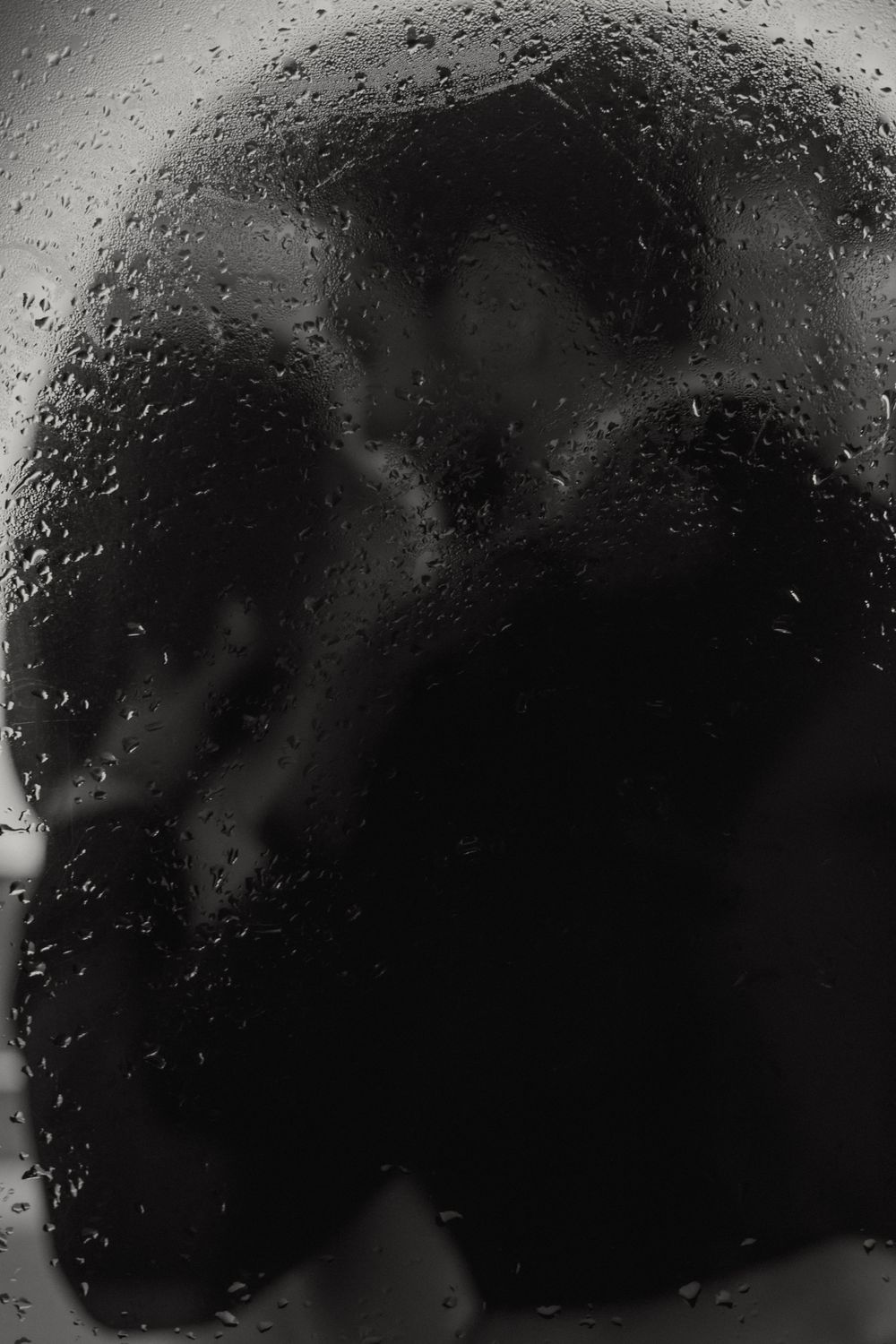 A silhouette appears as a dark shape behind a glass surface covered in water droplets and condensation.