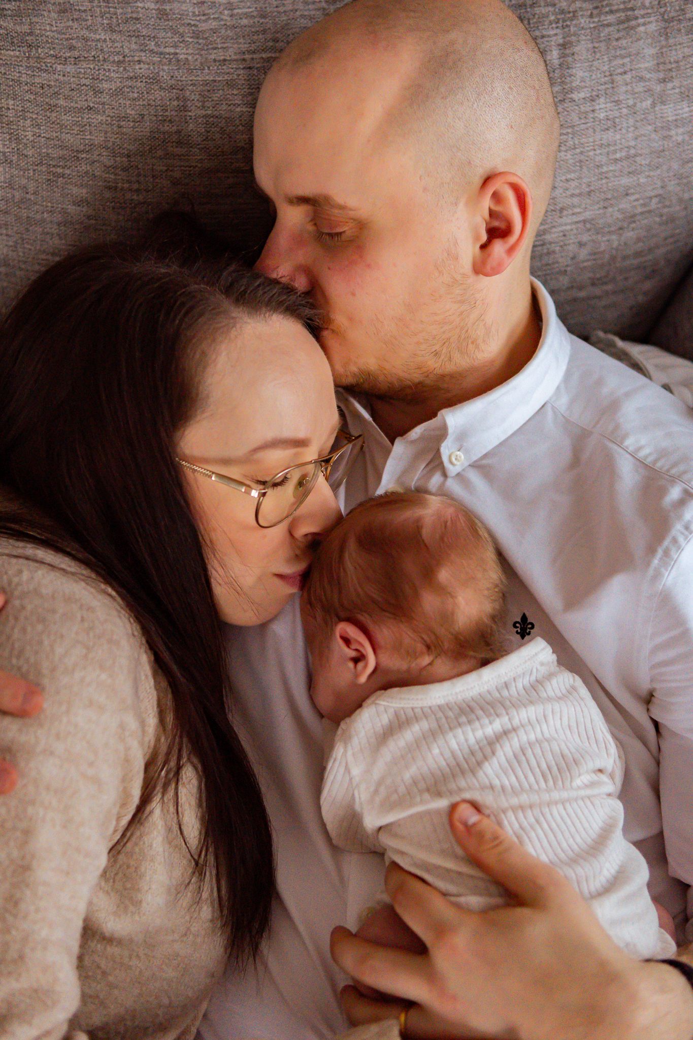 Kärleksfull och intim stund mellan föräldrar och nyfödd bebis som ligger tätt intill varandra i soffan. Fotograf, nyföddfotograf, Umeå