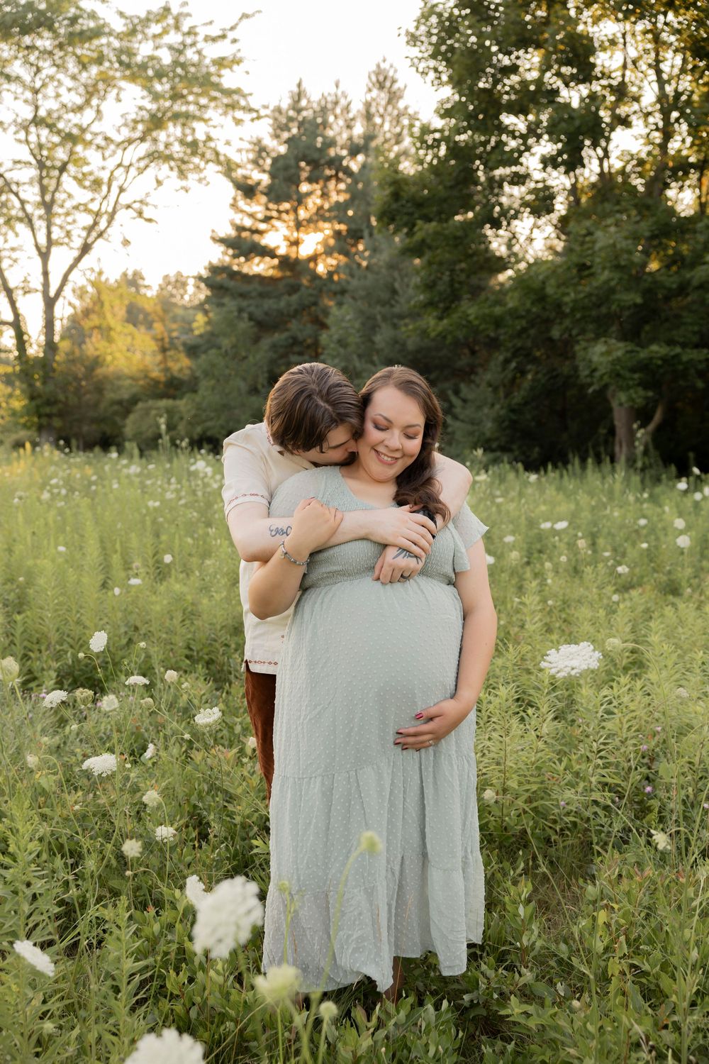 A couple shares a tender moment in a wildflower meadow in metro Detroit at sunset during a maternity photoshoot