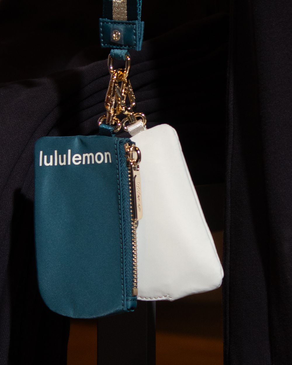 Teal and white Lululemon accessory bag hanging with gold chain detail.