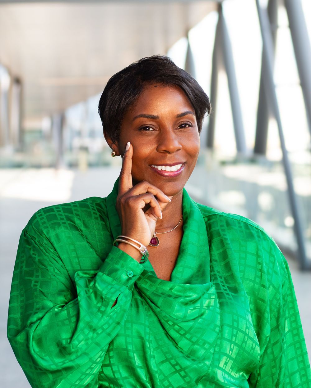 Professional headshot of person in bright green silk blouse against modern architectural background.